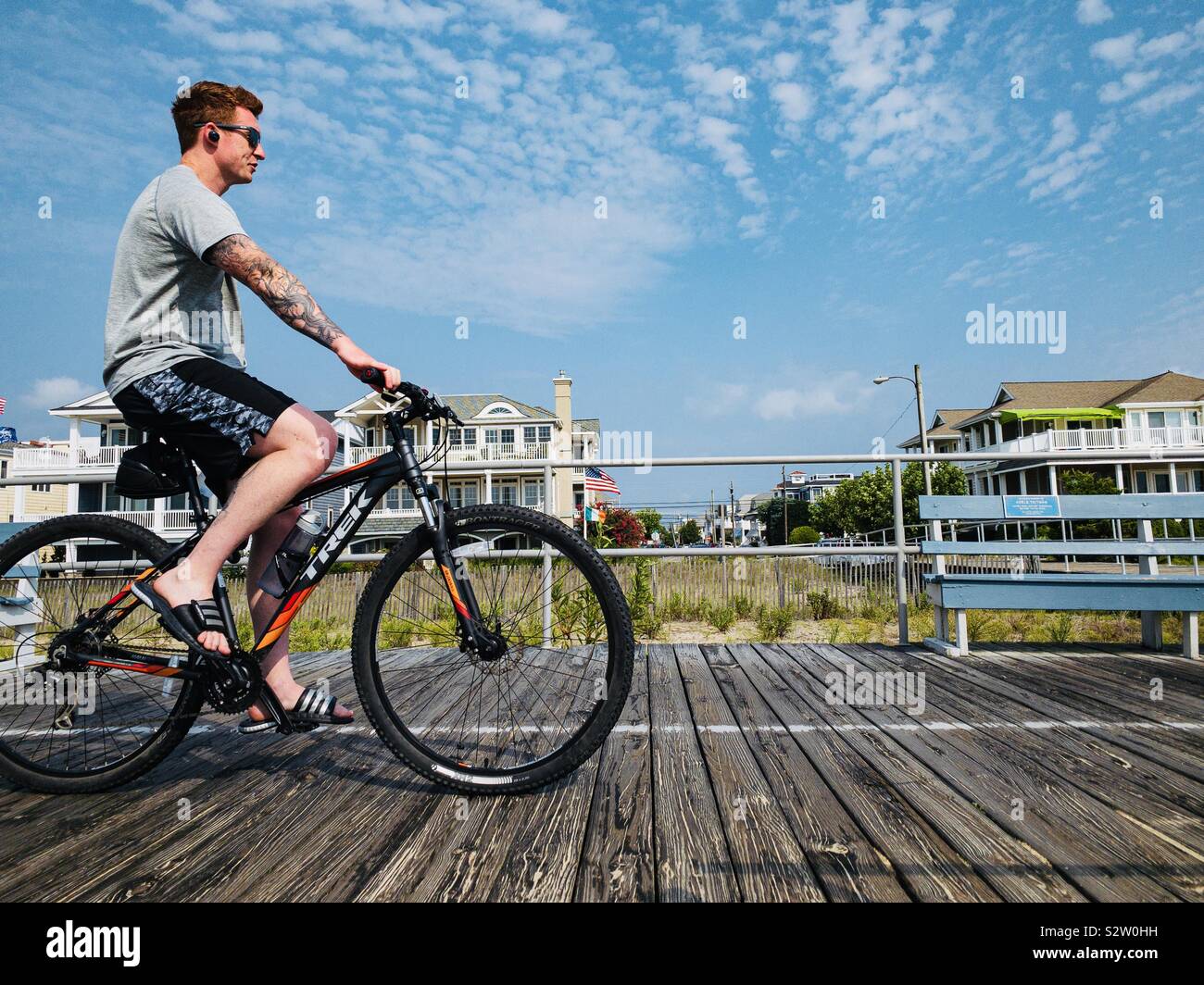 Man with tattoos Cycling on boardwalk with beach houses , Ocean City, New Jersey, USA - Smartphone Captured Stock Image