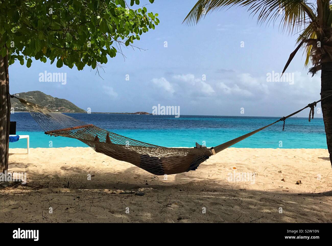 Man in Hammock Relaxing in the Shade Of Two Trees On Palm Island In The Grenadines Stock Photo