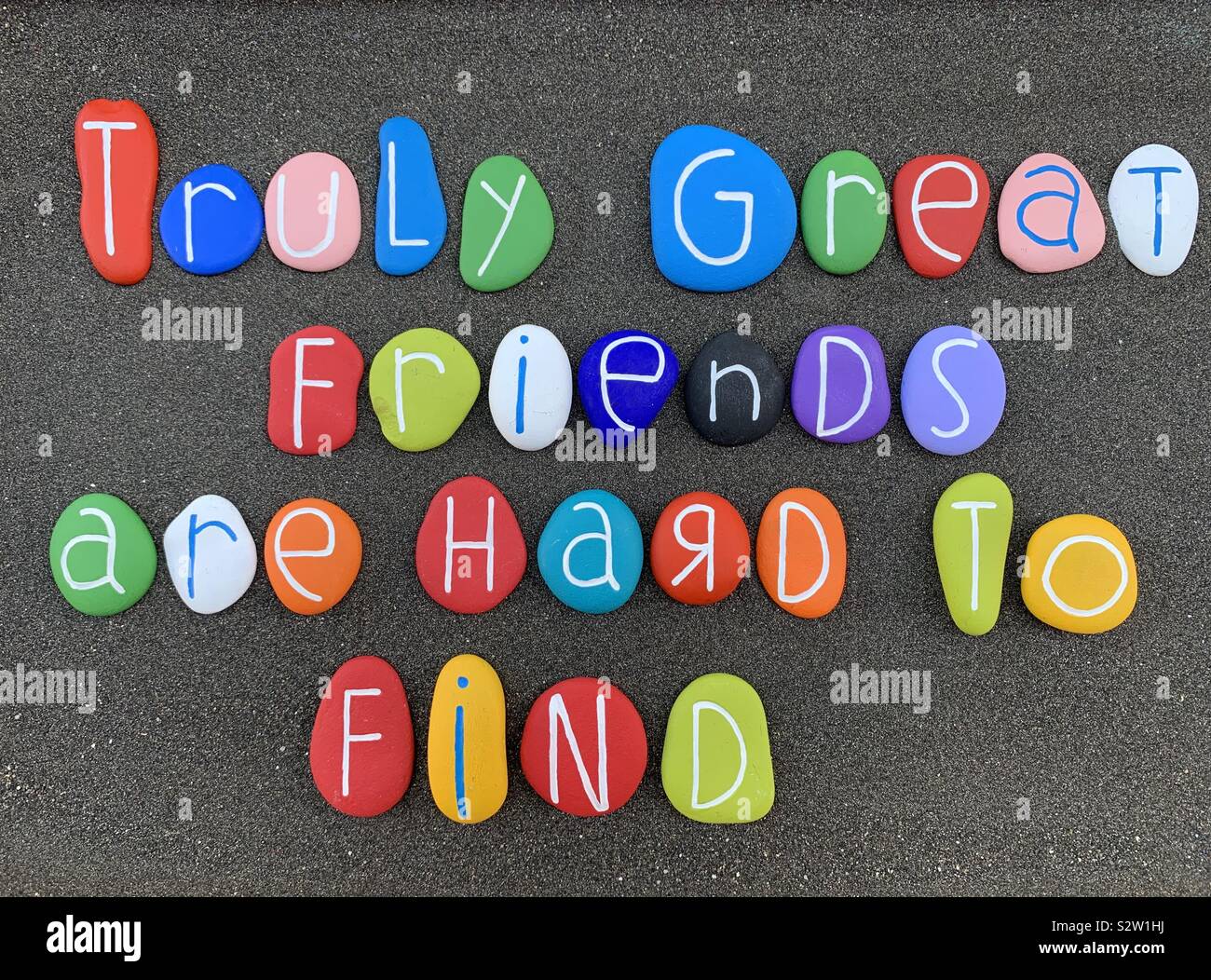 Truly great friendsare hard to find, wordsof wisdom composed with multi colored stone letters over blackvolcanic sand - Smartphone Captured Stock Image