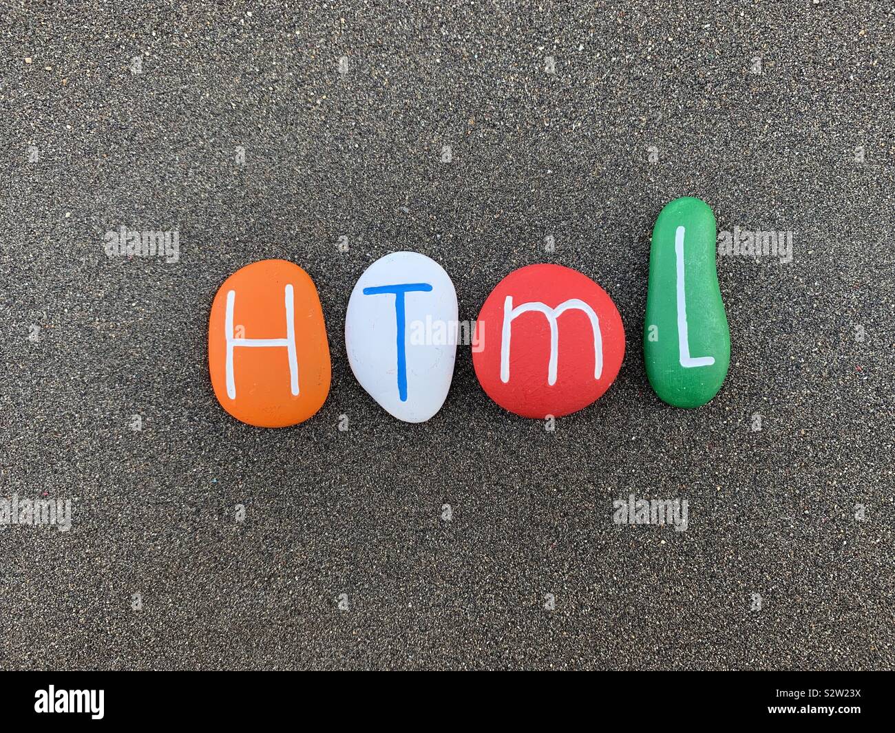 HTML, HyperText Markup Language composed with colored stones over black volcanic sand Stock Photo