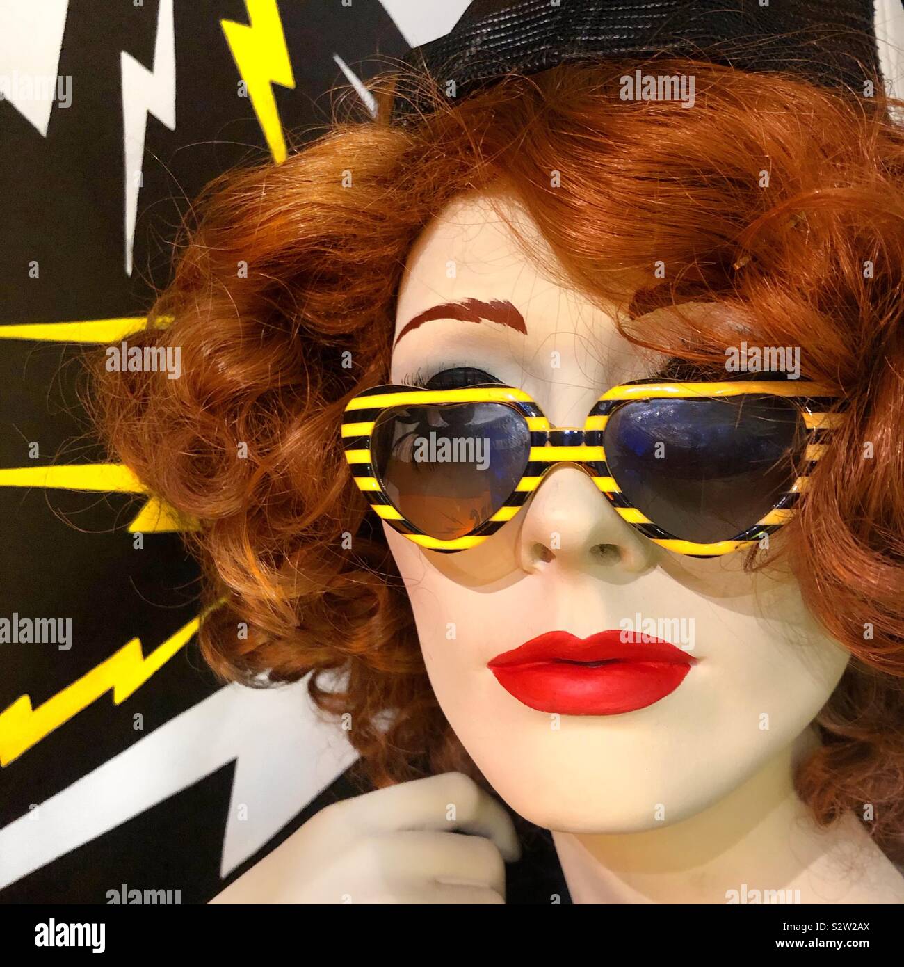 A closeup of a red haired mannequin with red lips and sunglasses Stock Photo