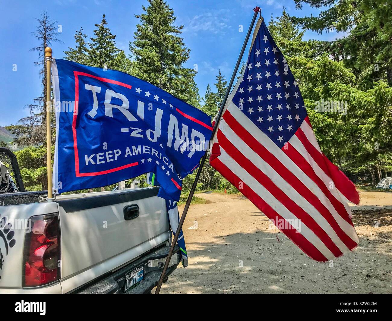 Trump 2020 campaign flag and United States flag fly from the back of a white pickup on the Fourth of July Stock Photo
