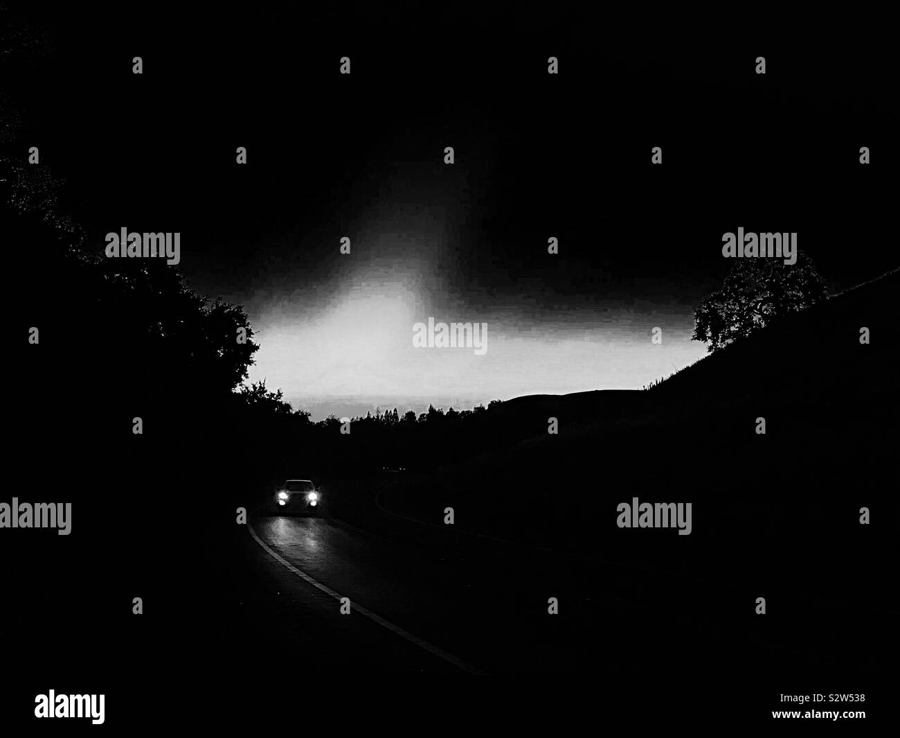 Automobile traveling on road at dusk, in black and white Stock Photo