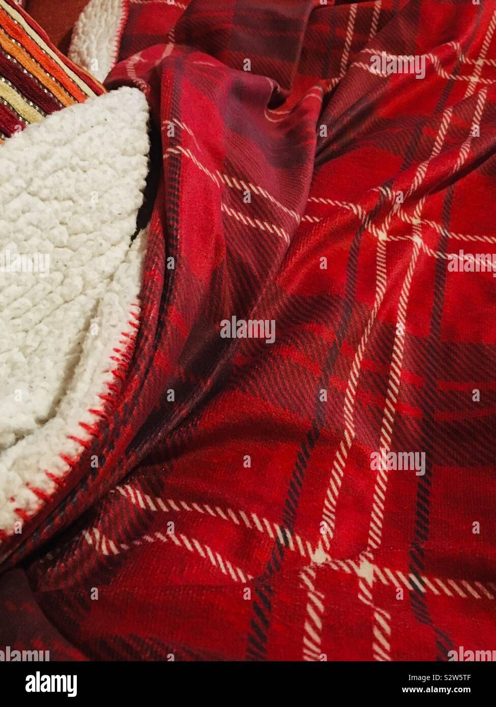 Autumnal coloured tartan blanket with cushion ready for a cozy afternoon on the sofa. - Autumn afternoons of Hygge Stock Photo