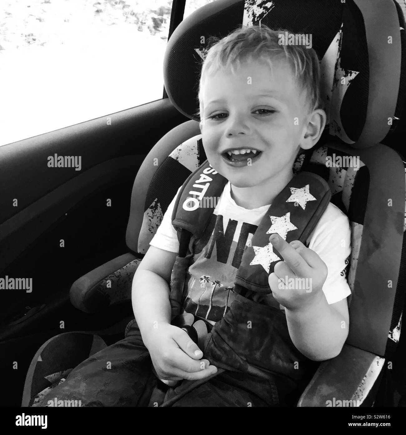Two year old boy in a car seat sticking up his middle finger. Stock Photo
