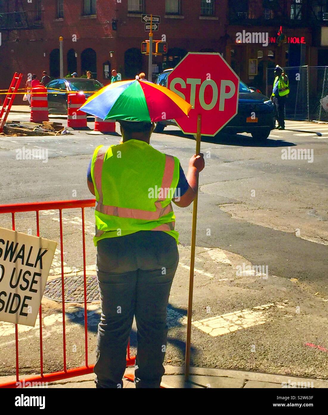 Female day laborer wearing a whimsical head umbrella at a curbside construction site in Murray Hill, NYC, USA - Smartphone Captured Stock Image