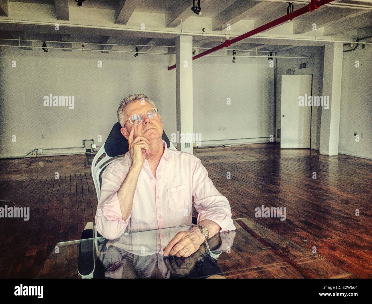 Senior man contemplating life at a desk in a nearly empty office area, USA - Smartphone Captured Stock Image