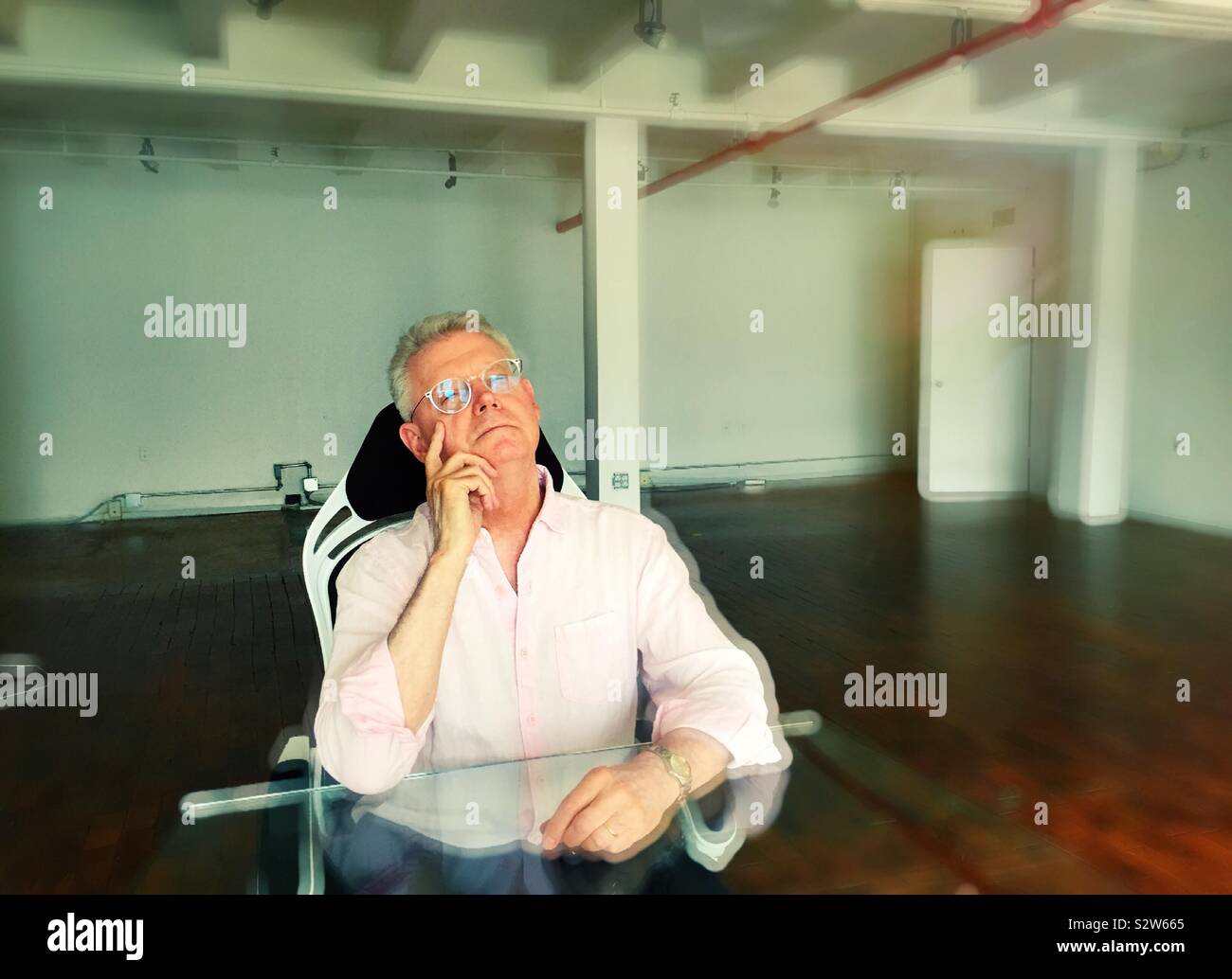 Contemplative senior man thinking about his next step in an empty office space, USA - Smartphone Captured Stock Image