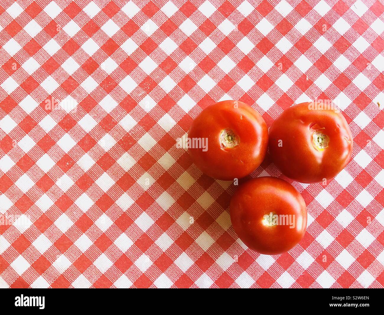 Three large red tomatoes on a red and white checked background Stock Photo
