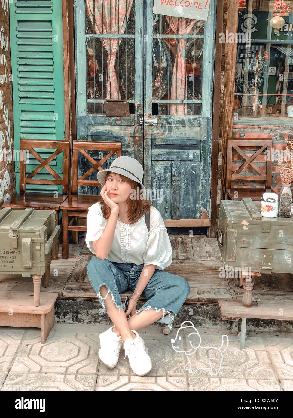 a-girl-sitting-in-front-of-a-vintage-coffee-shop-with-her-imaginary-dog-taken-in-hanoi-train-street-vietnam-S2W6KY.jpg
