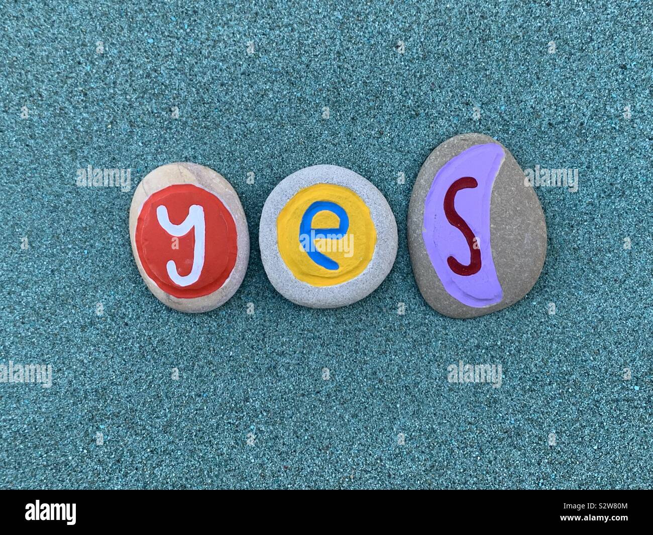 Yes text composed with colored stone letters over green sand - Smartphone Captured Stock Image