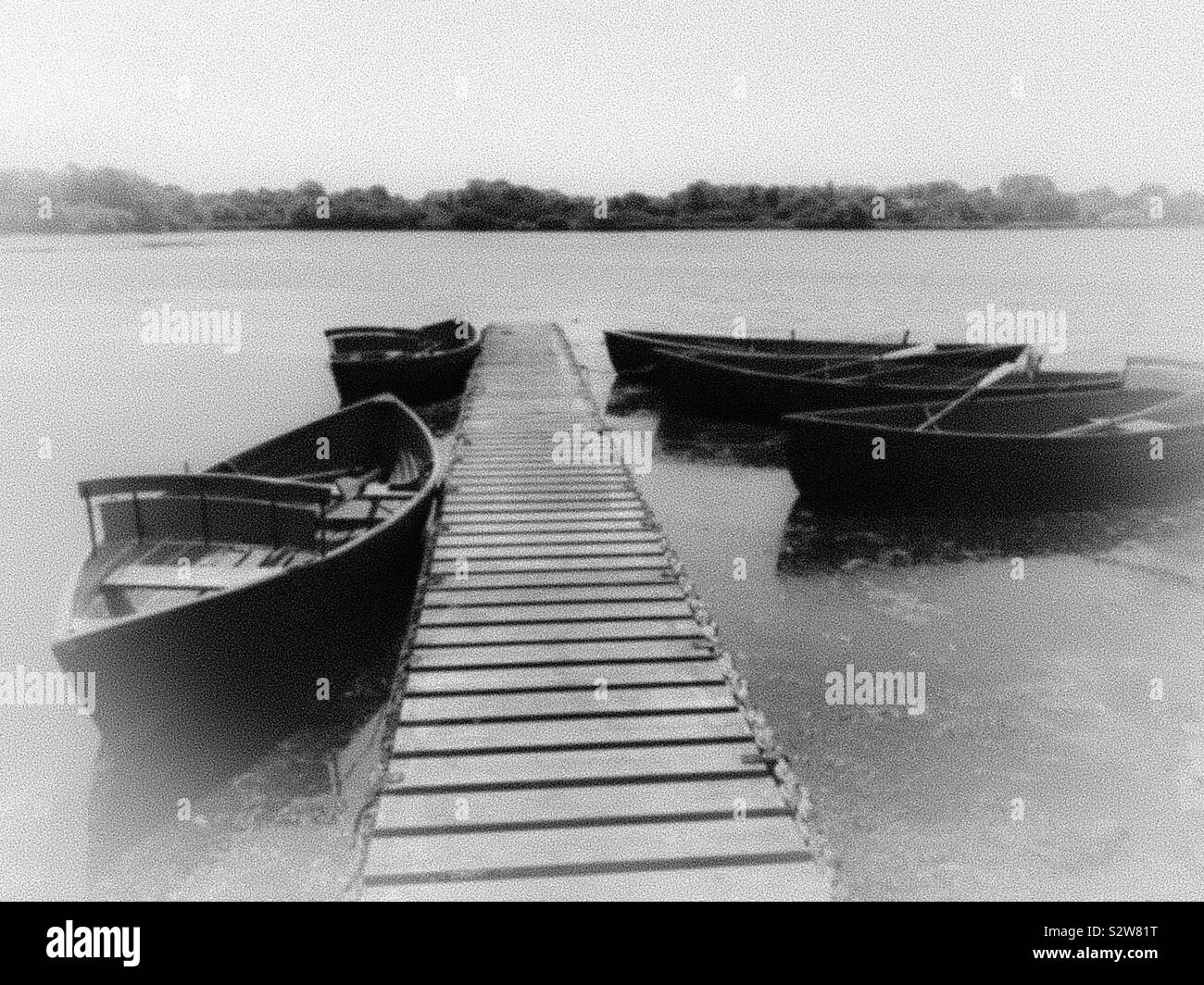 Black and white shot of pleasure boats tied up along a wooden jetty, with added mist effect. - Smartphone Captured Stock Image