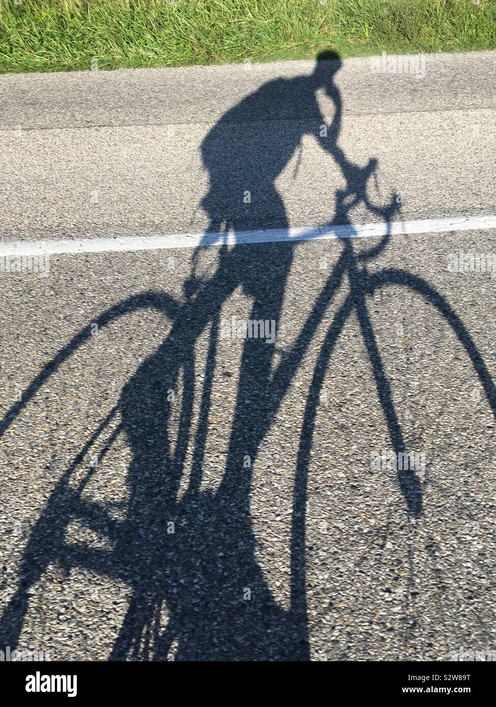 Shadow of a cyclist riding his bike in France, and using mobile phone at the same time, which is dangerous on a cycle. - Smartphone Captured Stock Image