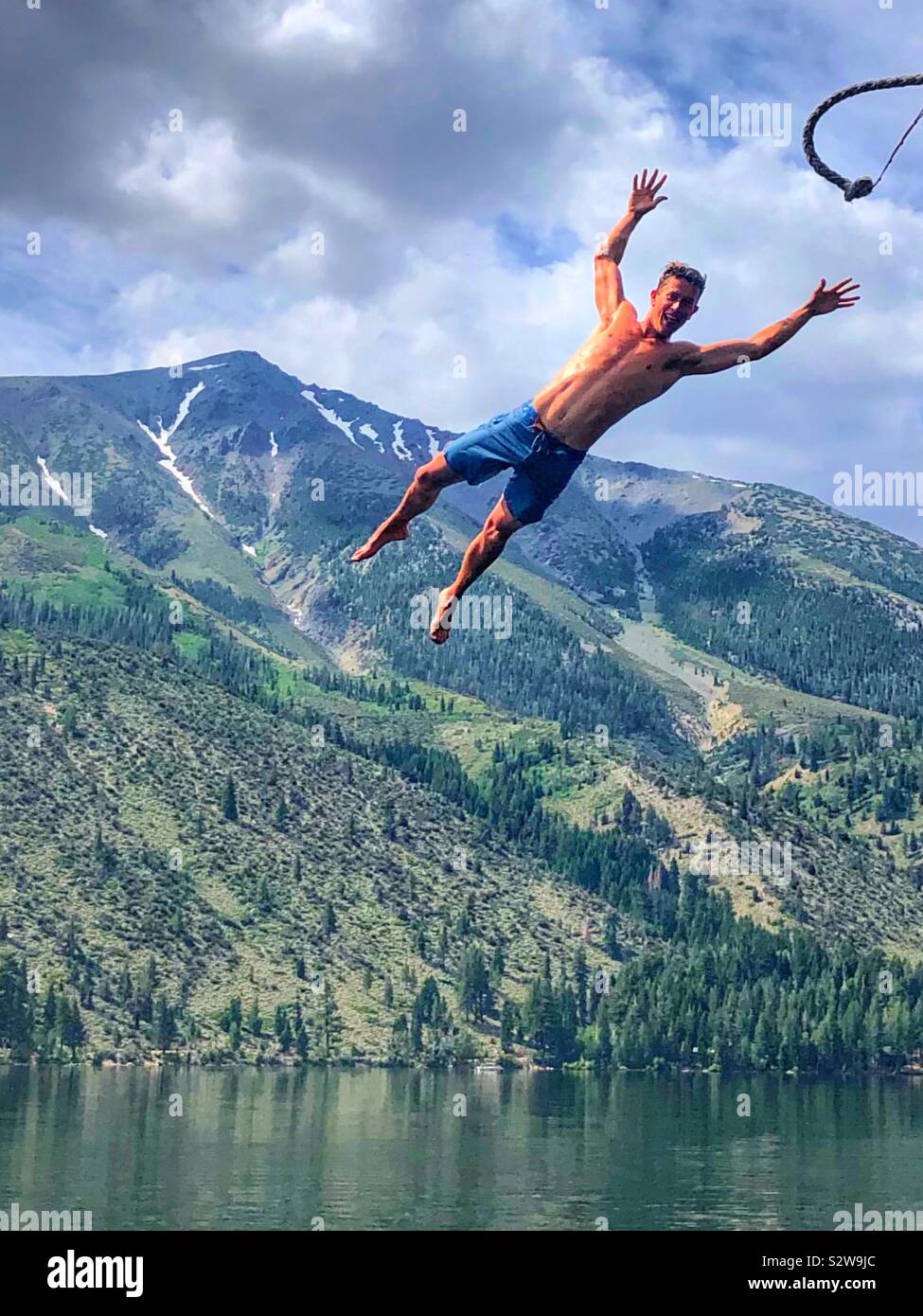 Young millennium jumping off a rope swing while on vacation in the mountains on a lake Stock Photo