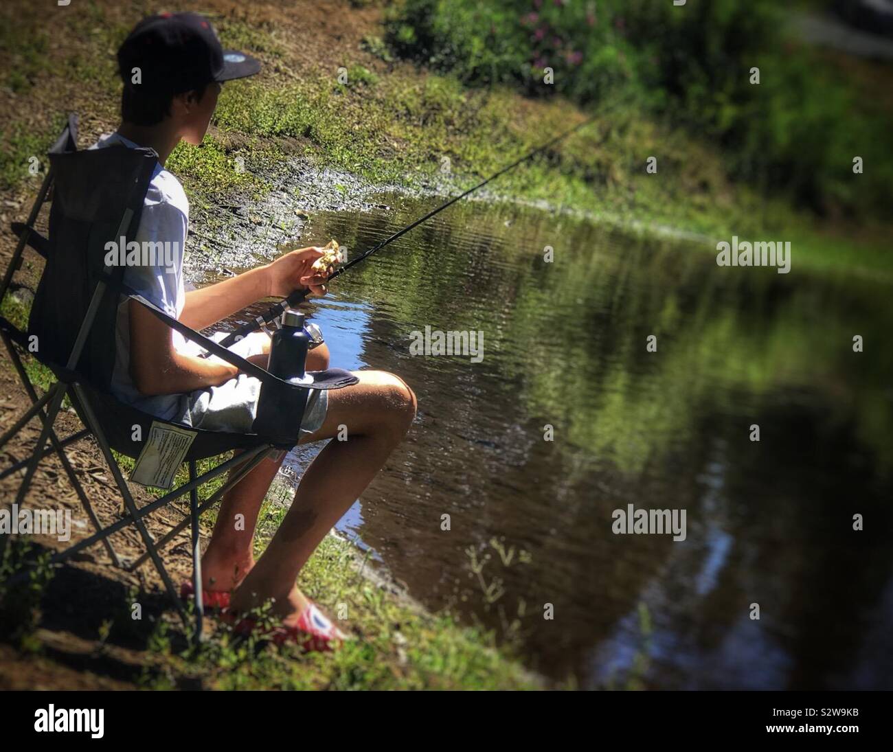 https://c8.alamy.com/comp/S2W9KB/teenage-boy-sitting-in-a-chair-while-fishing-along-the-shoreline-S2W9KB.jpg