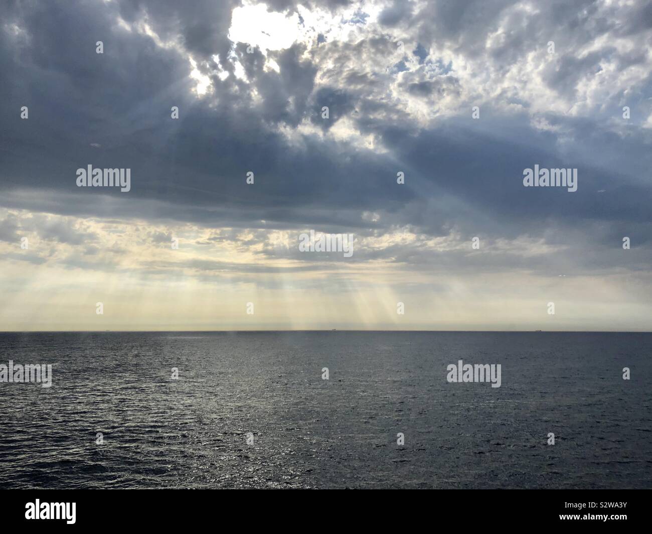Sunlight shining through clouds over sea Stock Photo