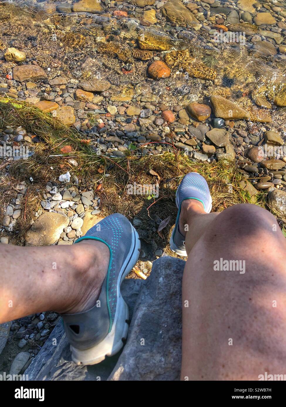 A woman sitting on a rock on the waterfront. - Smartphone Captured Stock Image