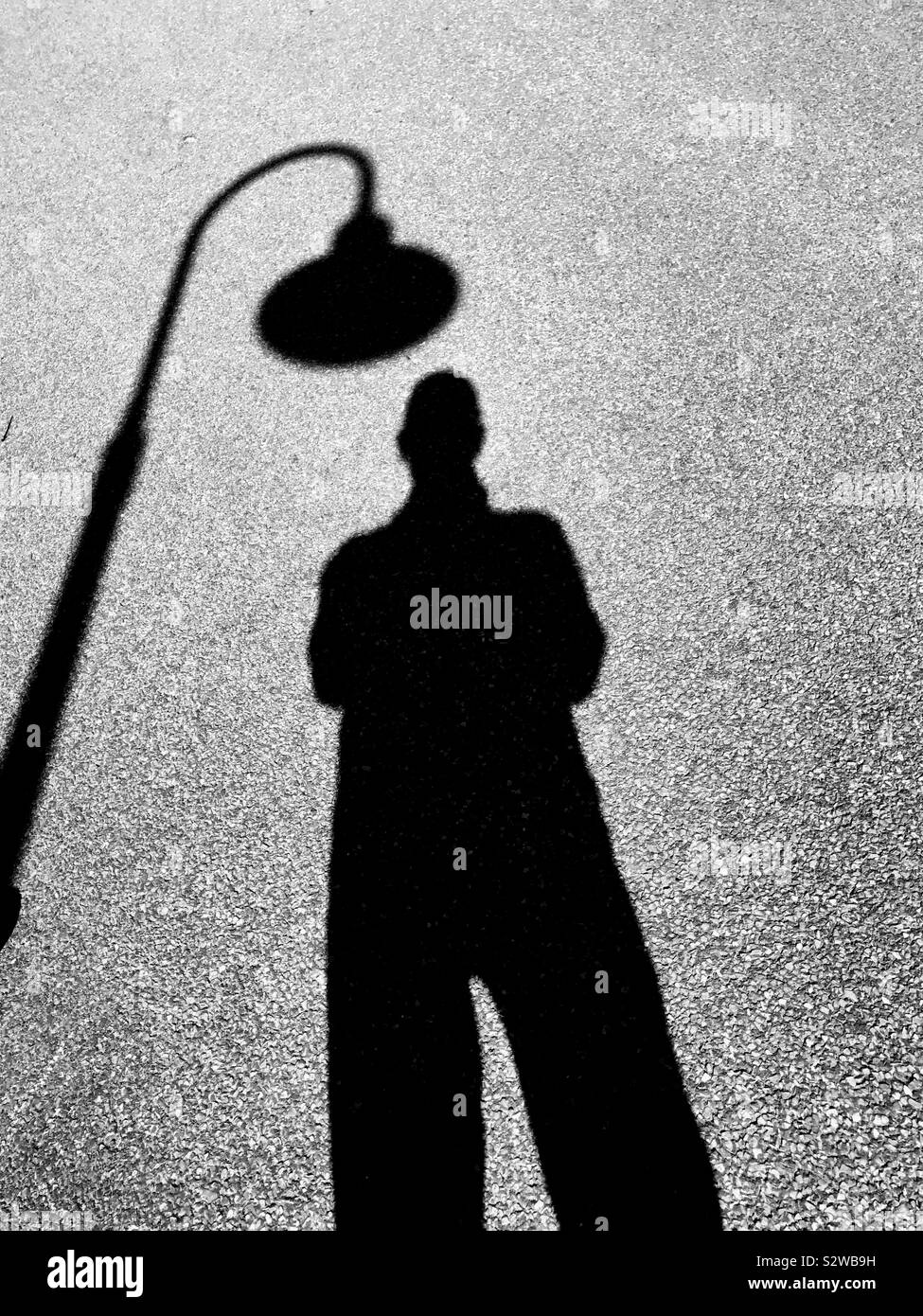 Man under street light silhouetted on pavement Stock Photo