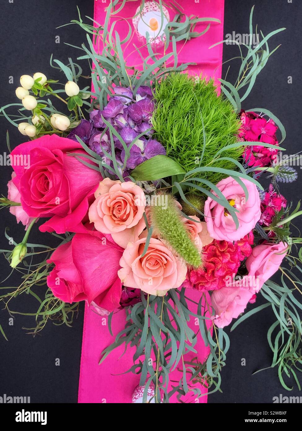 Beautiful flower arrangement with deep pink roses in full bloom on a black tablecloth. - Smartphone Captured Stock Image