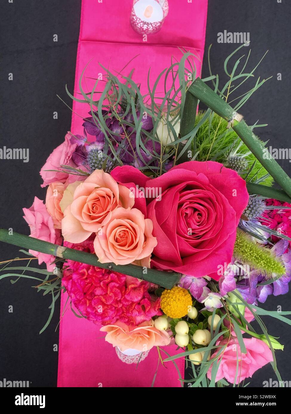 Beautiful flower arrangement with deep pink roses in full bloom on a black tablecloth. Stock Photo