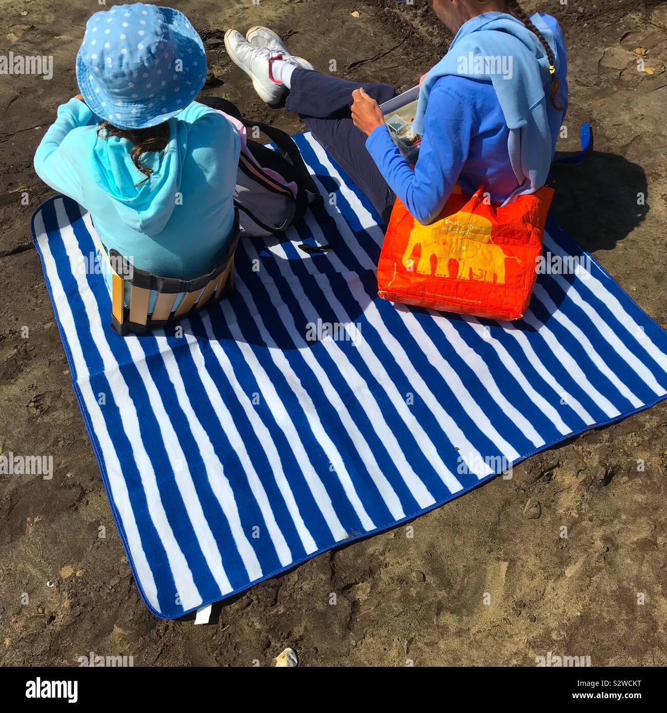 Two Women At The Beach Sitting On A Blue And White Striped