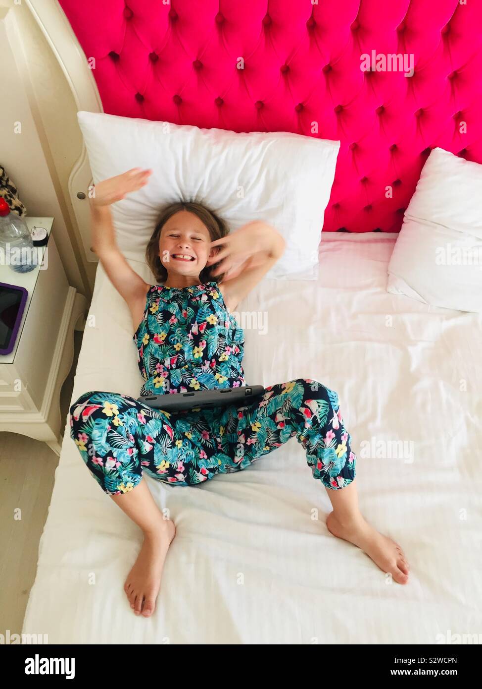 Female child playing on bed with iPad laughing and posing - Smartphone Captured Stock Image