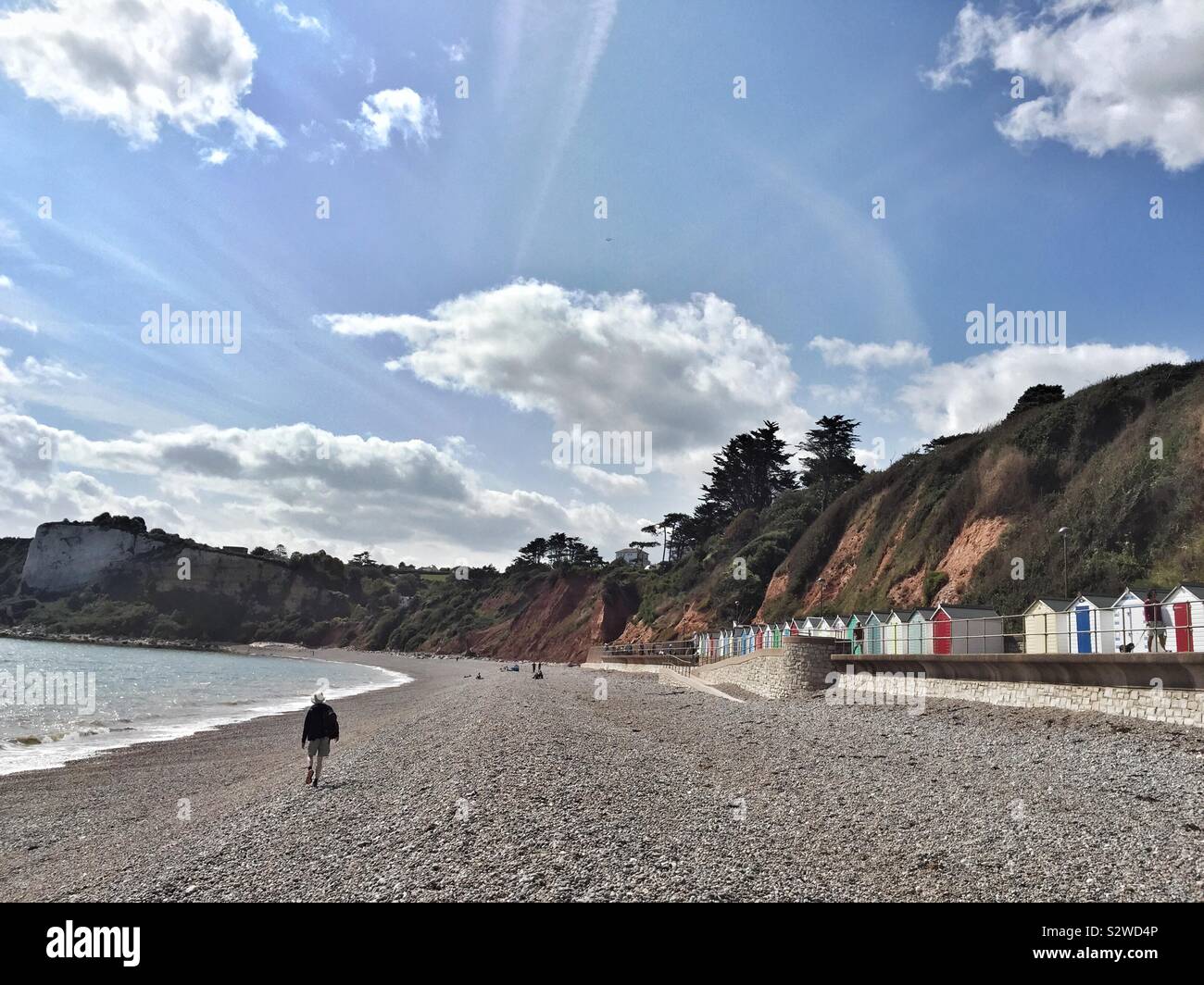 Cliffs and beach huts at Seaton, Devon, uk, with holiday maker walking along shingles - Smartphone Captured Stock Image