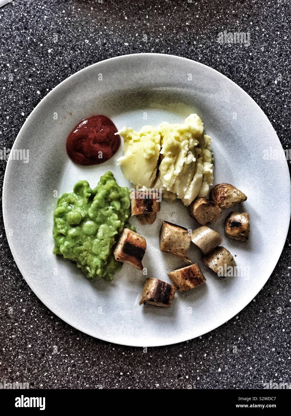 Veggie Sausage mash and mushy peas with ketchup served for a toddler