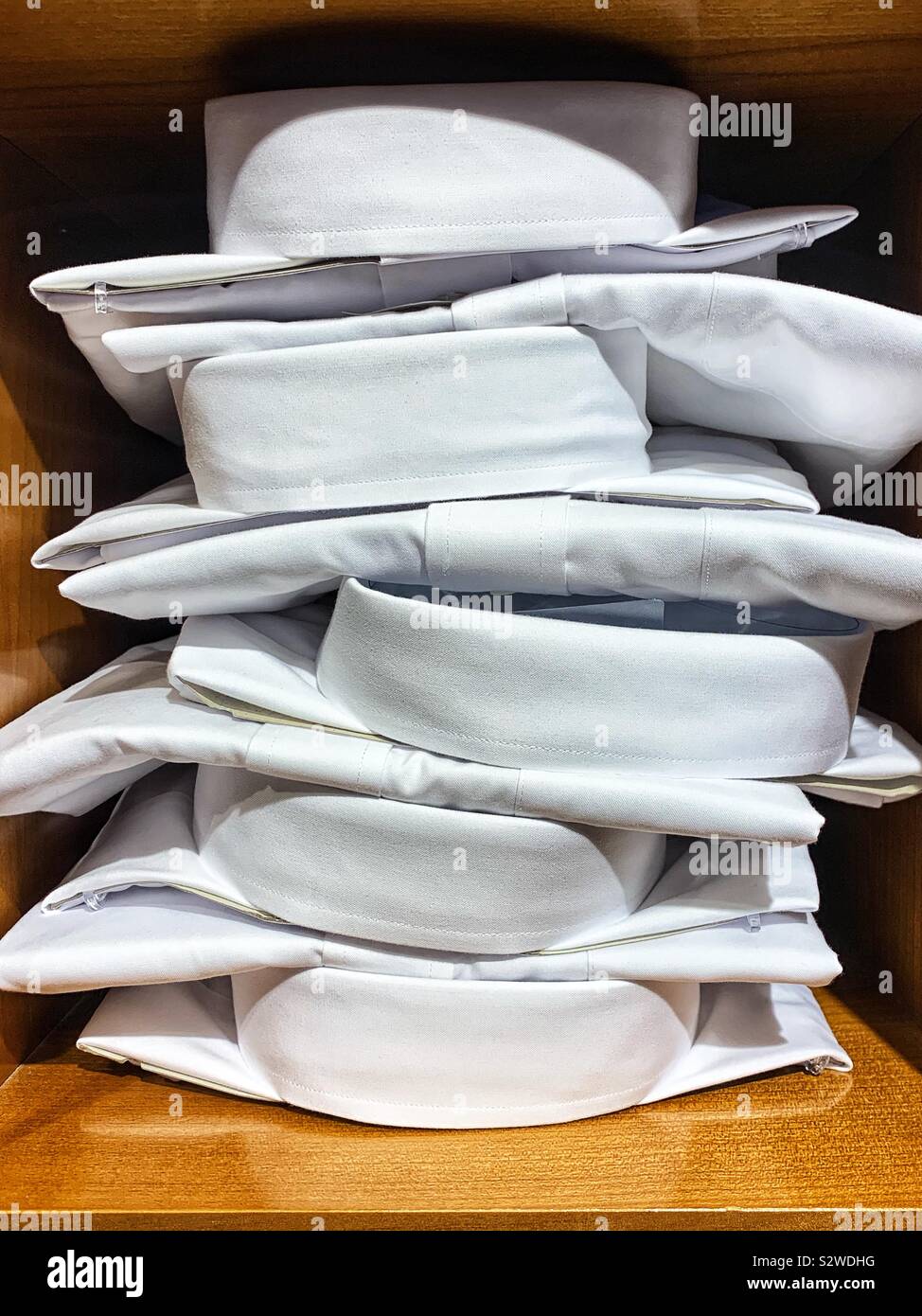Stack of folded white collared work shirts on wood shelves. - Smartphone Captured Stock Image