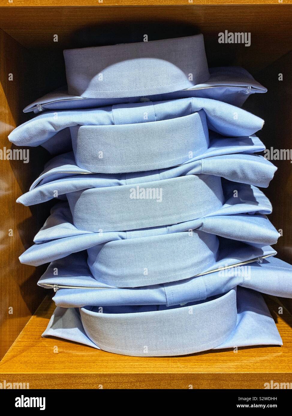 Stack of folded blue collared work shirts on wood shelves. - Smartphone Captured Stock Image