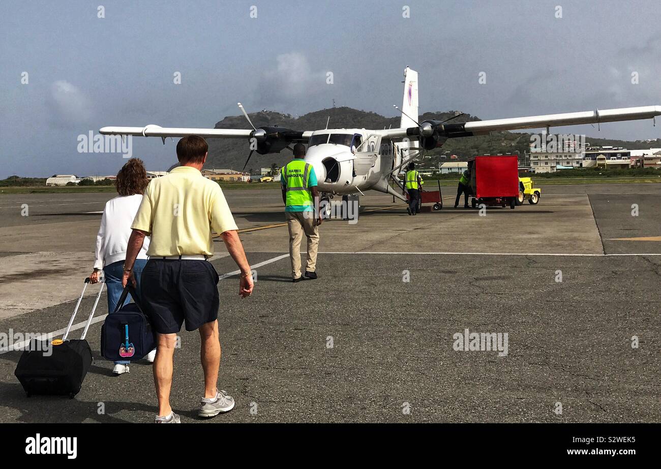 Passengers walking across the Tarmac to Grenadine Airways Aircraft that is being loaded by baggage Handlers - Hewanorra International Airport, St.Lucia West Indies Stock Photo