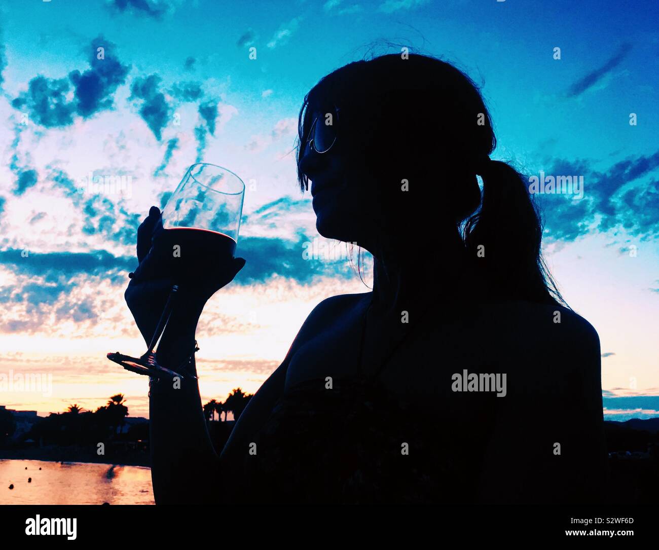 Silhouette of woman drinking wine at sunset on a beach in Ibiza. Summer holiday - Smartphone Captured Stock Image