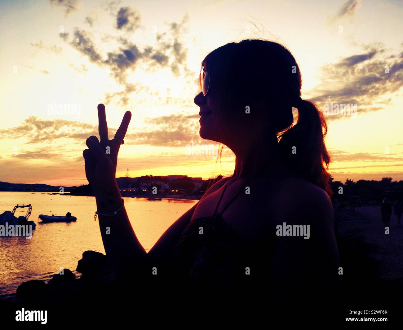 Silhouette of woman making peace sign on beach in Ibiza at sunset. Hippy woman. Love and peace. Chill out Ibiza - Smartphone Captured Stock Image