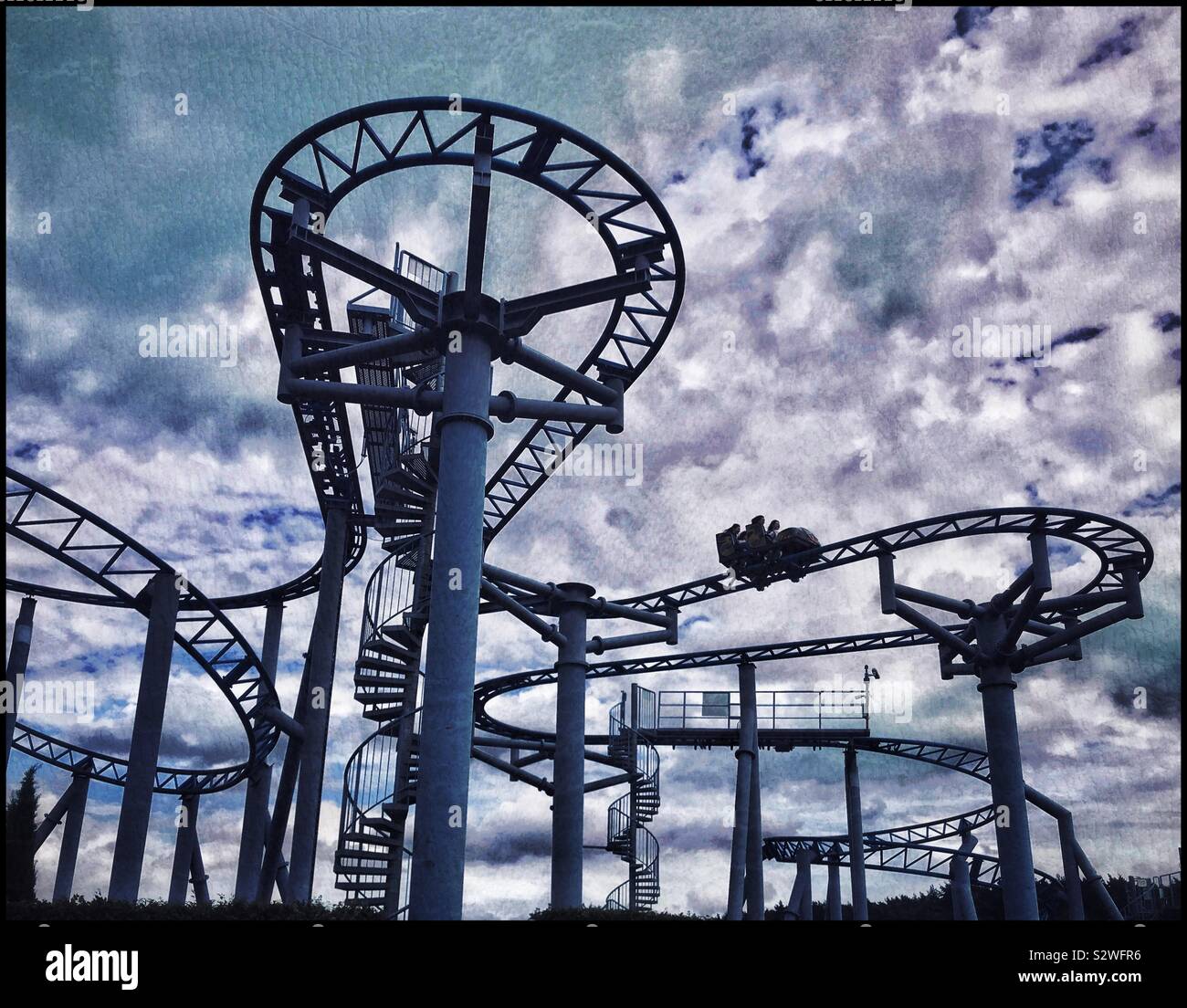 A group of people ride on a roller coaster ride at a theme park. An atmospheric picture - dark clouds and sinister colours or just winter holiday fun? Photo Credit-© COLIN HOSKINS. - Smartphone Captured Stock Image