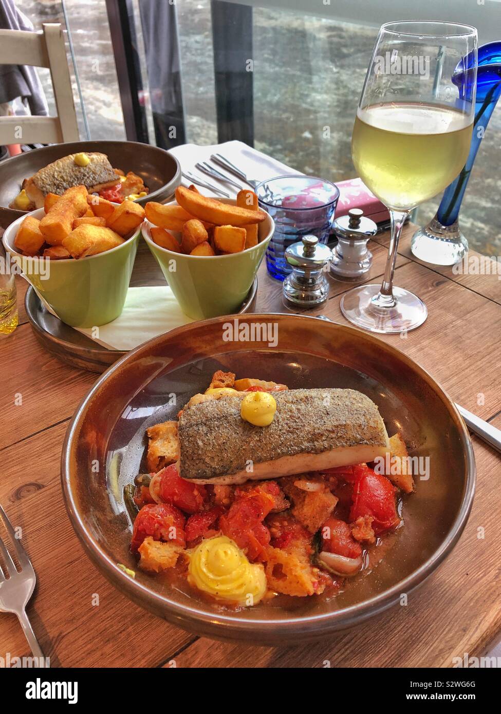 Salted hake, panzanella salad and fries with a cold glass of Chardonnay. Stock Photo