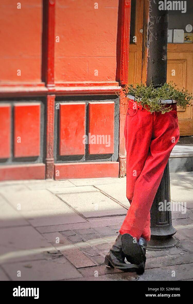 A pair of red trousers and black shoes are used to house a plant and is supported by a metal post outside a shop in Madrid’s trendy district of Malasaña Stock Photo