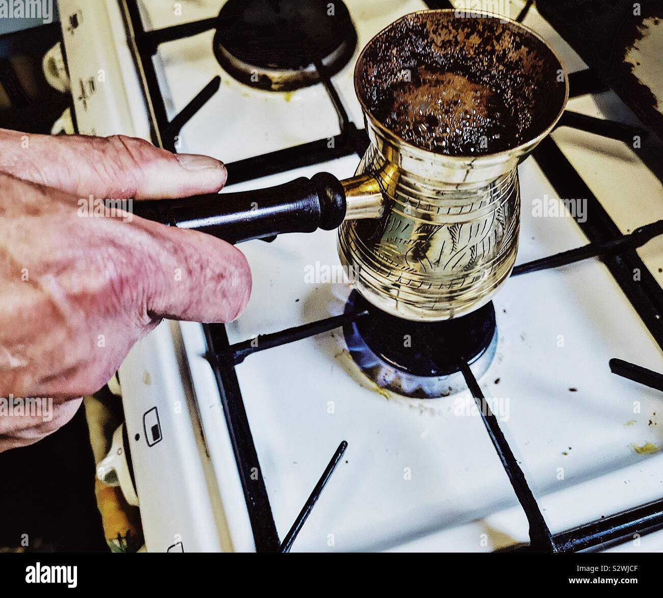 Man making Lebanese coffee in traditional brass coffee pot. Called a rakweh in Arabic it is narrower at the top to allow the foam or achoueh to form - Smartphone Captured Stock Image