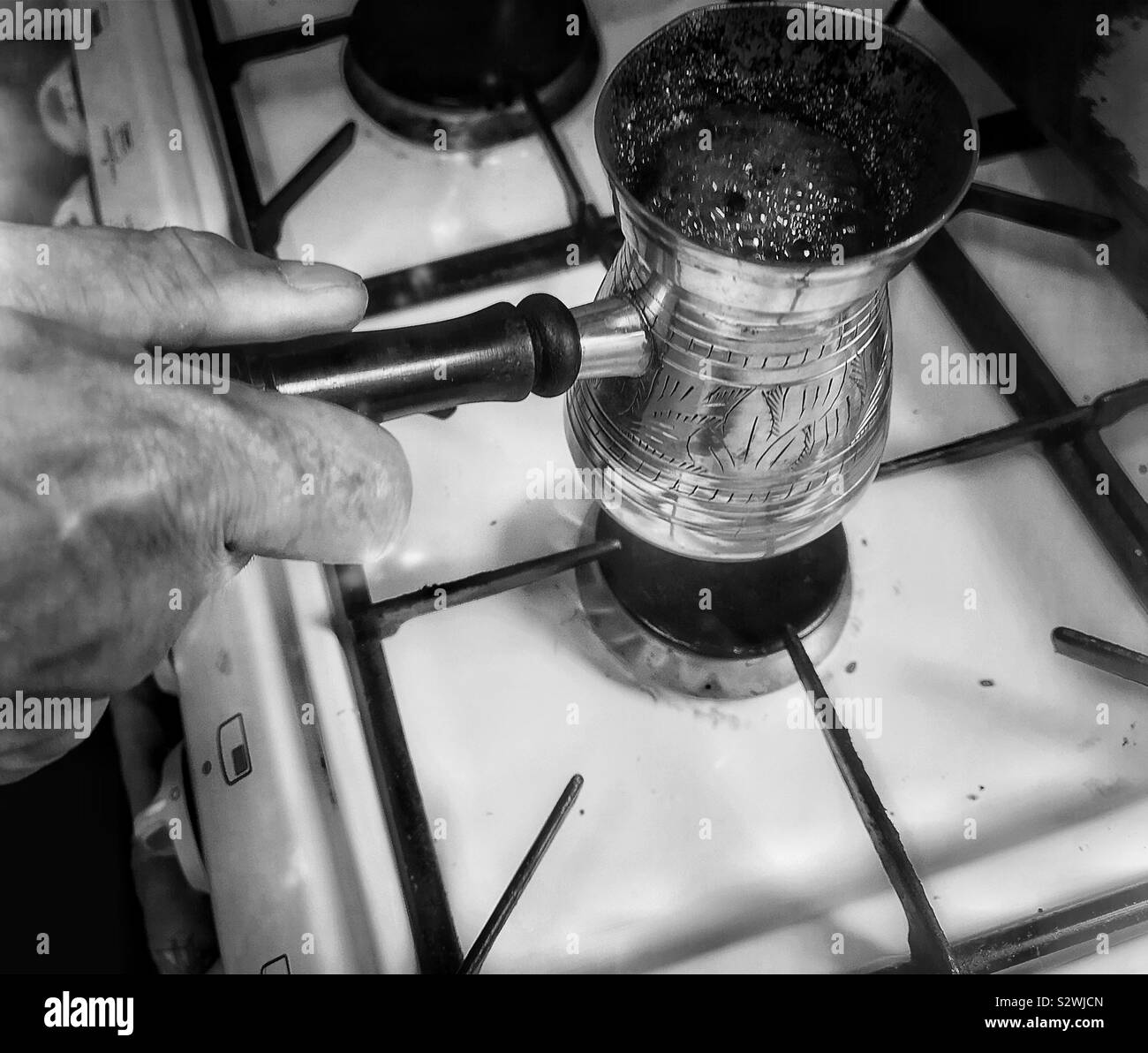 Man making Lebanese coffee in traditional brass coffee pot. Called a rakweh in Arabic it is narrower at the top to allow the foam or achoueh to form - Smartphone Captured Stock Image