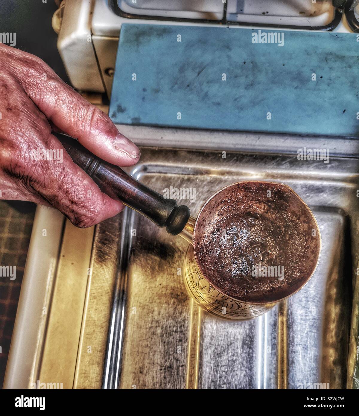 Man making Lebanese coffee in traditional brass coffee pot. Called a rakweh in Arabic it is narrower at the top to allow the foam or achoueh to form - Smartphone Captured Stock Image
