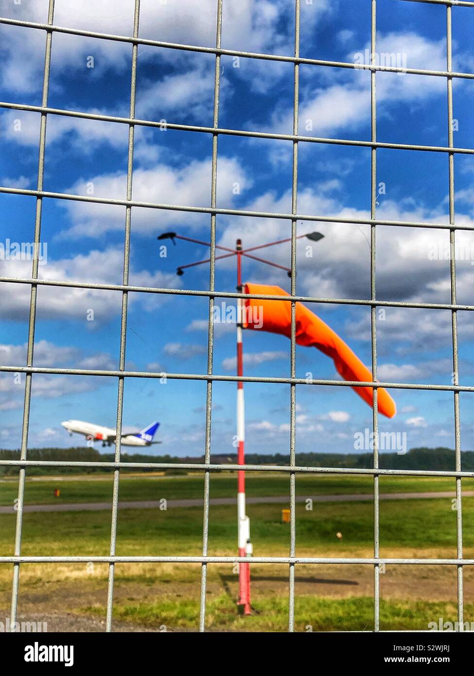 Airport perimeter fence with windsock and aeroplane taking off from runway Stock Photo