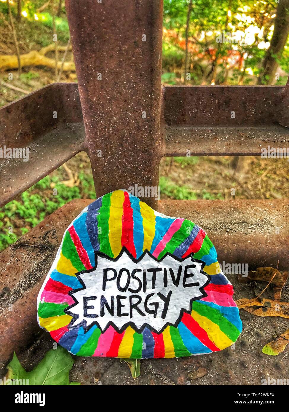A painted rock with the words positive energy leaning against a post on the landing of a set of stairs. Stock Photo