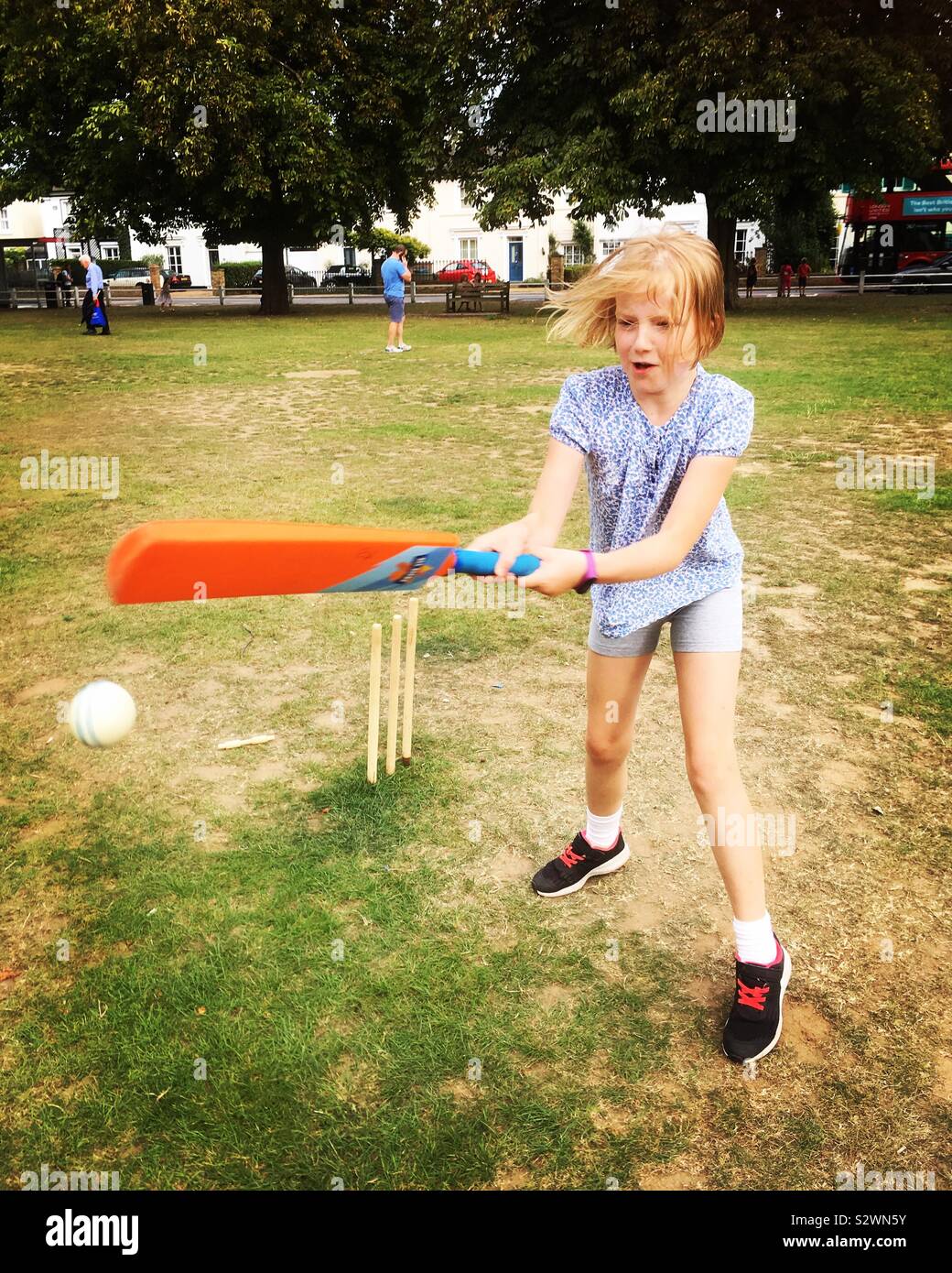 Nine year old girl / child plays cricket on the village green in a game of childrens cricket with other kids Stock Photo