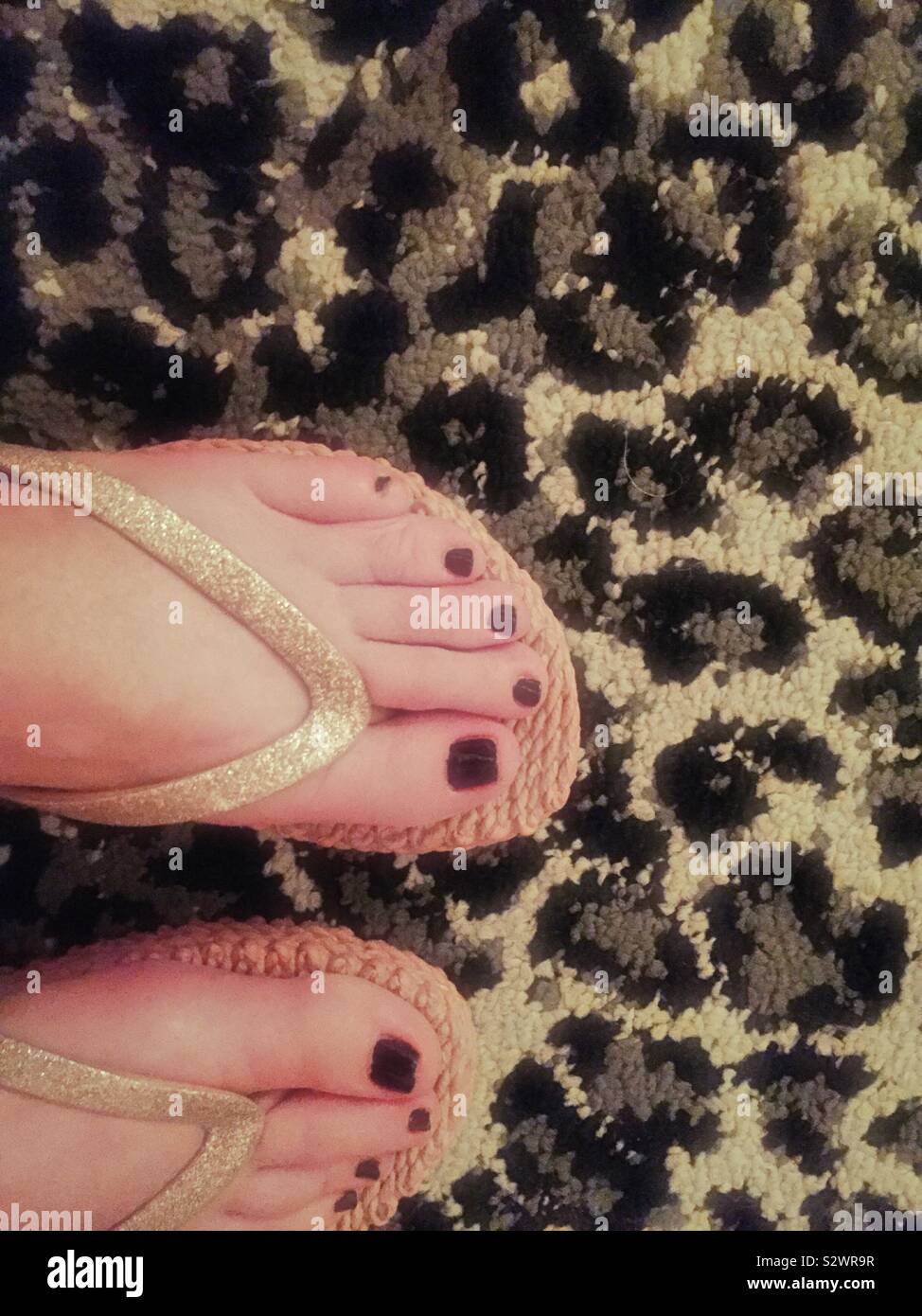 Close up of freshly applied red nail polish on a Caucasian woman feet on top of a leopard pattern carpet, USA - Smartphone Captured Stock Image