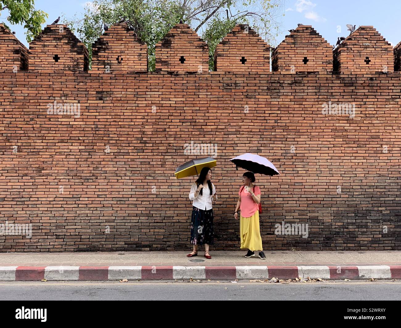 Two Thai women with umbrellas in front of historic city wall, Chiang Mai, Thailand - Smartphone Captured Stock Image