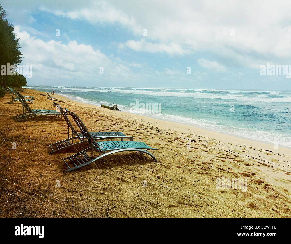 Empty beach chairs on sandy seaside beach on cloudy day. Travel, vacation concept of tropical escape. Stock Photo
