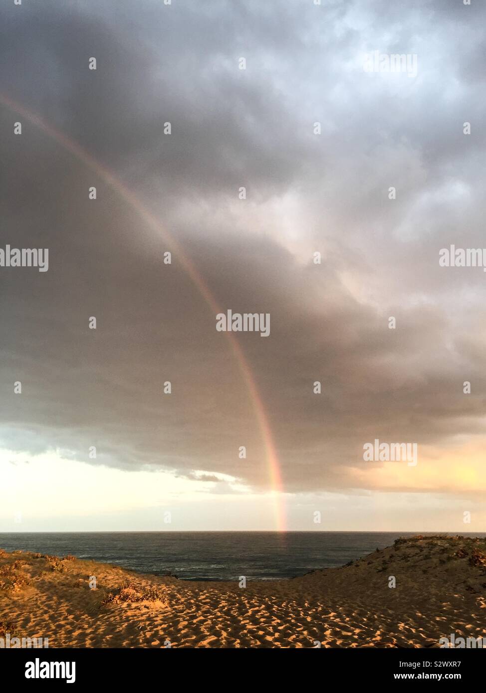 Rainbow over the ocean at sunrise in South-West France. Stock Photo
