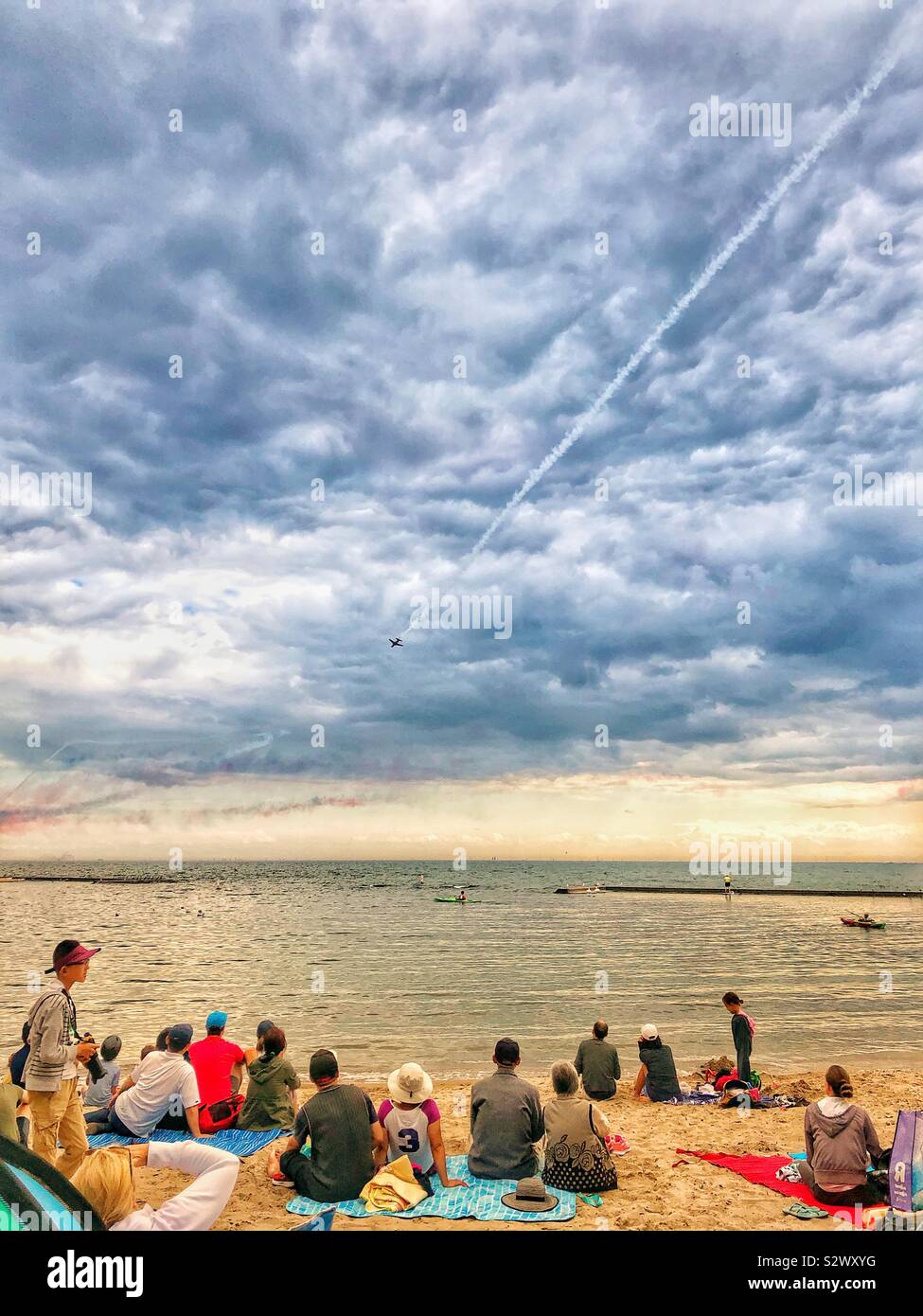 People sitting on a beach in Toronto watching the air show. - Smartphone Captured Stock Image