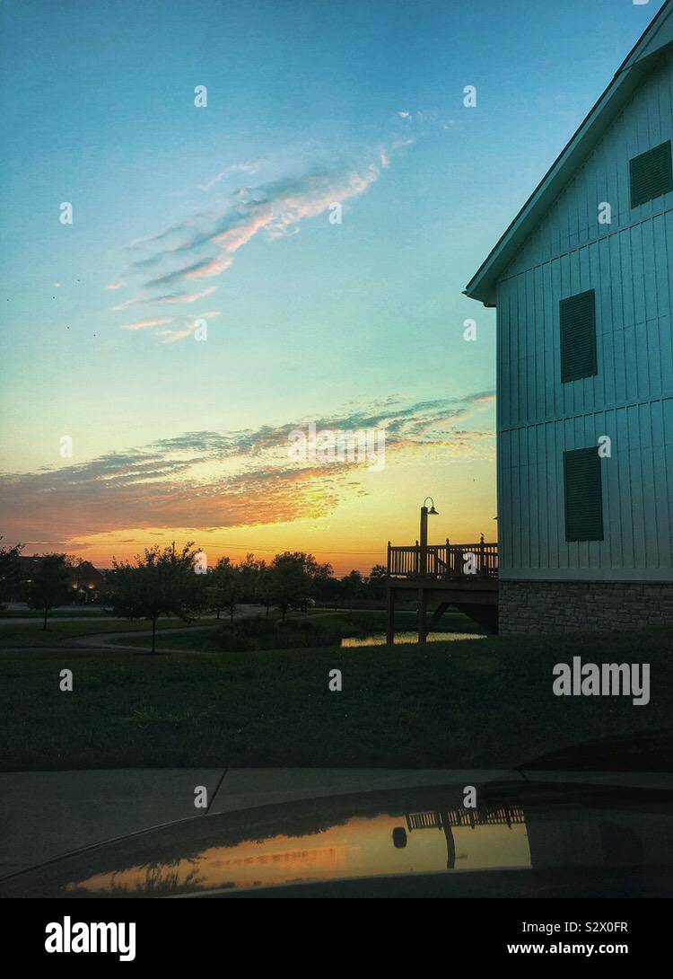 A photo, shot from a car, of a sunset and barn.  The sunset is reflecting off if the car hood in the foreground and a pond in the background. A Mextures filter was used. - Smartphone Captured Stock Image