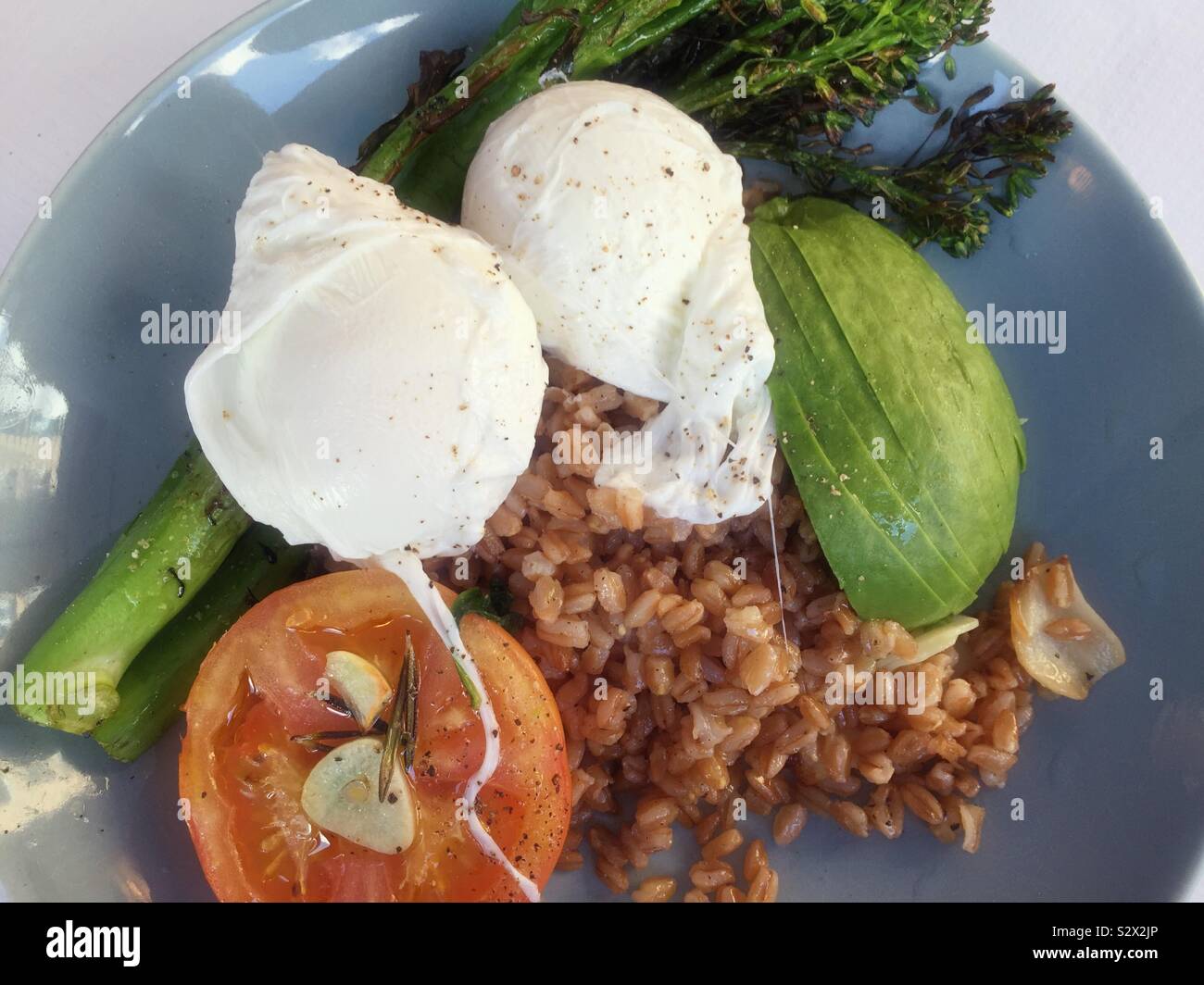Gourmet meal of poached eggs on a bed of warm Farro grains with tomatoes, avocados and broccolini accompaniments Stock Photo