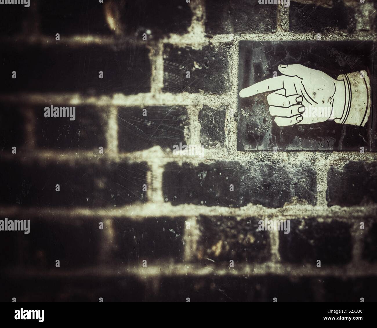Tile on a brick wall with an illustration of a pointing finger on it in Hampstead, London - Smartphone Captured Stock Image